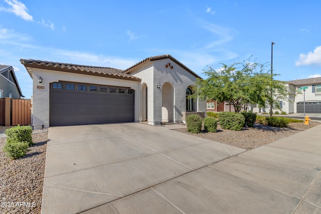 mediterranean / spanish home with stucco siding, driveway, a garage, a tiled roof, and fence