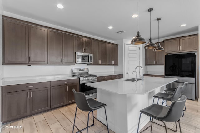 kitchen with appliances with stainless steel finishes, a sink, a kitchen bar, recessed lighting, and dark brown cabinetry
