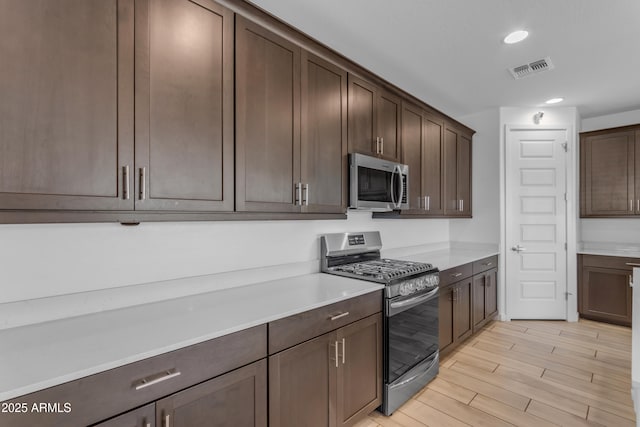 kitchen with appliances with stainless steel finishes, dark brown cabinets, light countertops, recessed lighting, and light wood-type flooring