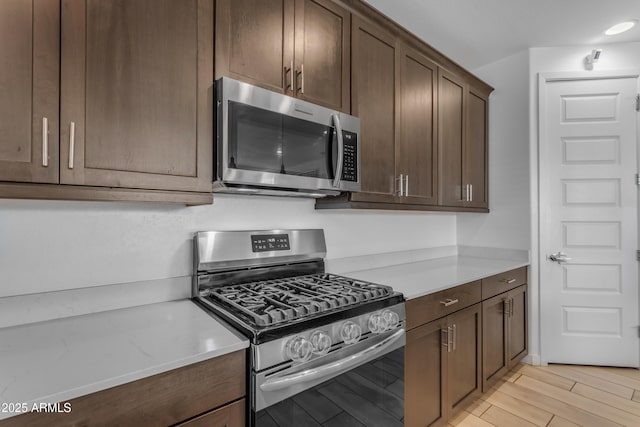 kitchen with stainless steel appliances, light countertops, dark brown cabinets, and light wood-style flooring