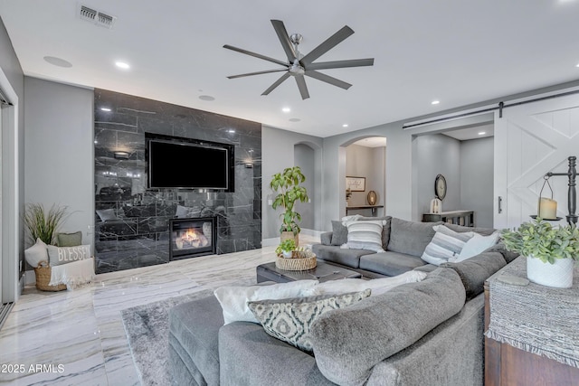 living room featuring a barn door, ceiling fan, and a high end fireplace