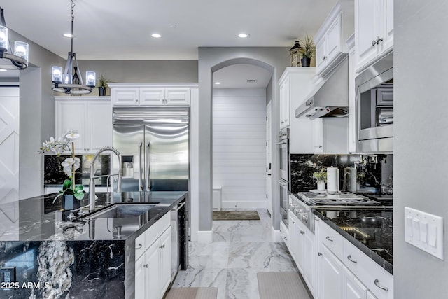 kitchen with dark stone countertops, sink, white cabinets, and hanging light fixtures