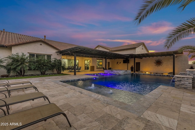 pool at dusk with pool water feature, an in ground hot tub, and a patio