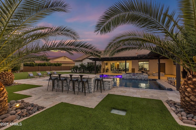 pool at dusk featuring an in ground hot tub, a bar, and a patio