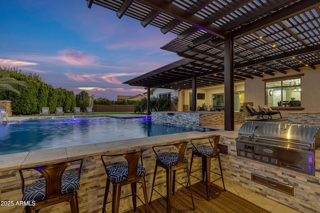 pool at dusk with grilling area, a pergola, exterior bar, pool water feature, and area for grilling