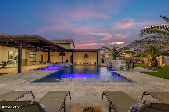 pool at dusk featuring a patio area, pool water feature, an outdoor bar, and an in ground hot tub