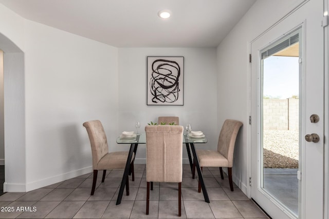 dining space with light tile patterned flooring, arched walkways, and baseboards