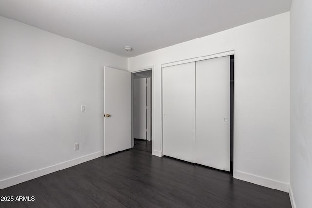 unfurnished bedroom with dark wood-style flooring, a closet, and baseboards