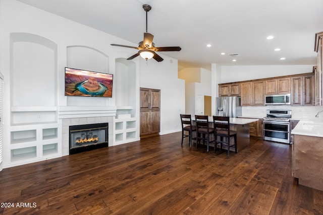 kitchen featuring appliances with stainless steel finishes, dark hardwood / wood-style flooring, a breakfast bar area, a tile fireplace, and a center island