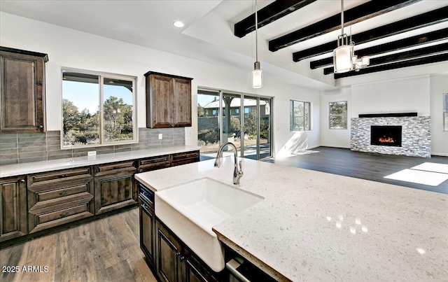 kitchen with a sink, light stone counters, tasteful backsplash, and beam ceiling