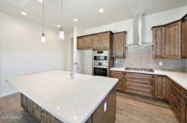 kitchen with wall chimney range hood, light stone countertops, a sink, stainless steel appliances, and backsplash