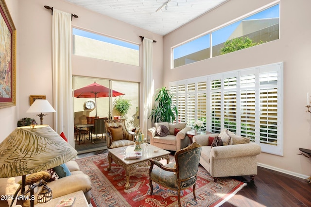 living room featuring dark wood-type flooring, a towering ceiling, and baseboards