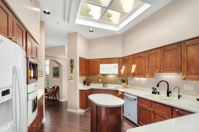 kitchen featuring white appliances, a kitchen island, a sink, light countertops, and brown cabinets