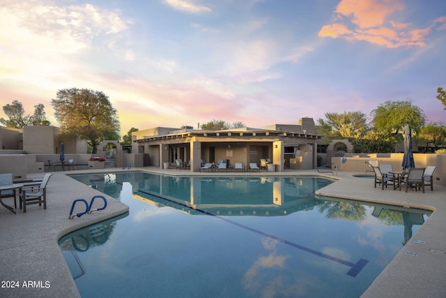 pool at dusk with a patio area and a community pool