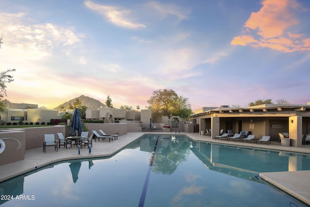 pool at dusk with a patio, a mountain view, and a community pool