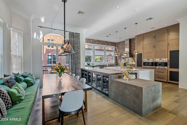 kitchen featuring ventilation hood, an island with sink, hanging light fixtures, oven, and hardwood / wood-style floors