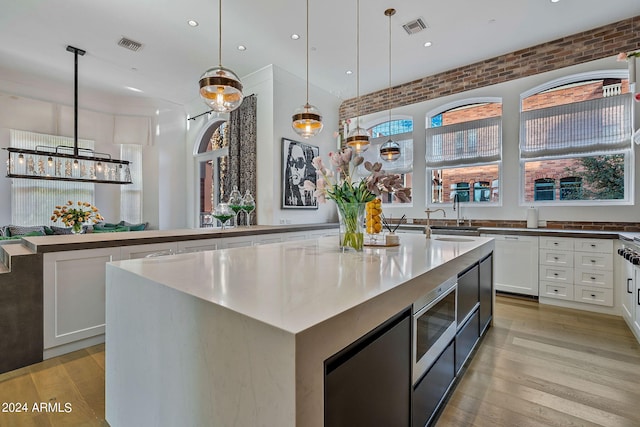 kitchen featuring stainless steel microwave, a kitchen island, light hardwood / wood-style flooring, and decorative light fixtures