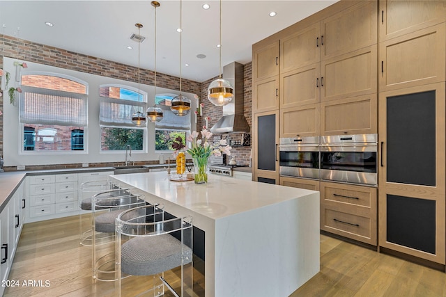 kitchen with hanging light fixtures, a kitchen island, stainless steel appliances, a kitchen bar, and wall chimney range hood