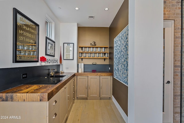 bar with light wood-type flooring, butcher block counters, brick wall, and sink