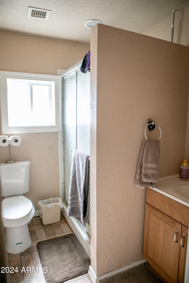 bathroom featuring toilet, tile floors, a shower with shower door, vanity, and a textured ceiling