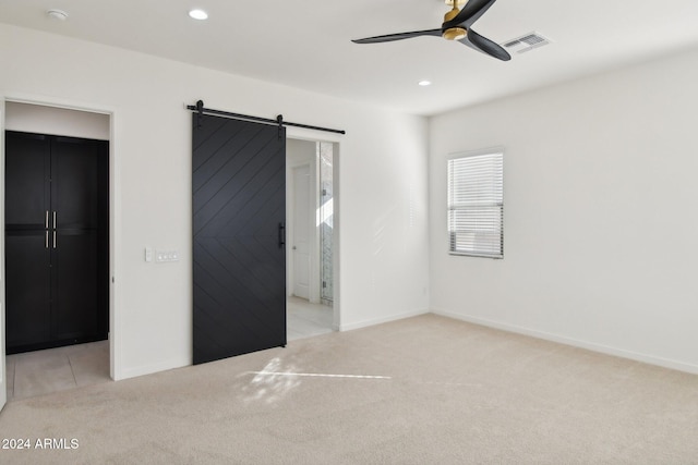 unfurnished bedroom with ensuite bath, light carpet, a barn door, and ceiling fan