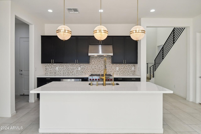 kitchen featuring wall chimney range hood, pendant lighting, and a kitchen island with sink