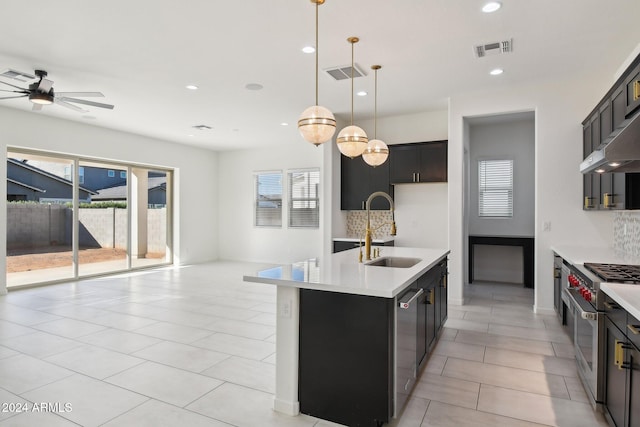 kitchen with tasteful backsplash, appliances with stainless steel finishes, decorative light fixtures, sink, and an island with sink