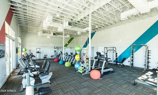 exercise room featuring a towering ceiling and dark carpet