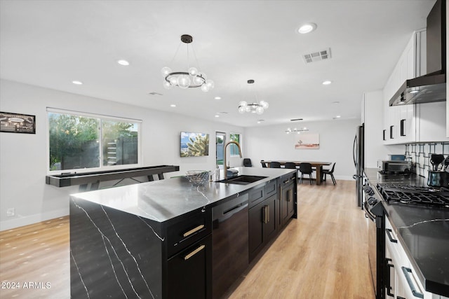 kitchen with stainless steel appliances, a kitchen island with sink, sink, light hardwood / wood-style flooring, and a chandelier