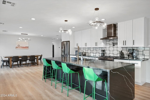 kitchen featuring white cabinetry, wall chimney range hood, stainless steel refrigerator with ice dispenser, pendant lighting, and a spacious island