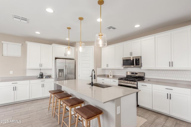 kitchen featuring white cabinetry, sink, a kitchen bar, hanging light fixtures, and stainless steel appliances