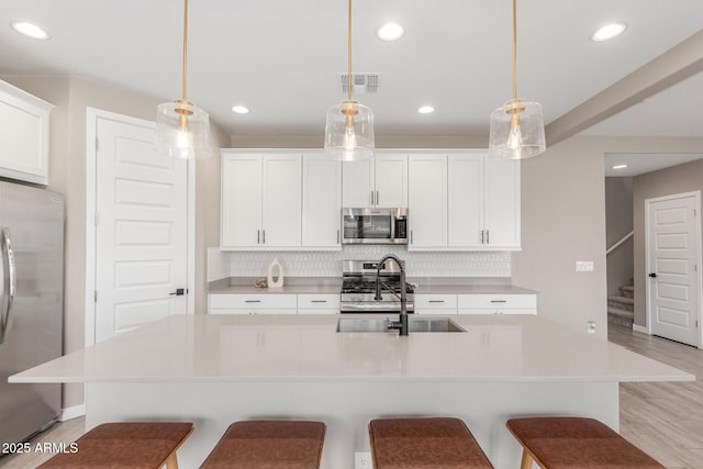 kitchen featuring an island with sink, appliances with stainless steel finishes, and pendant lighting