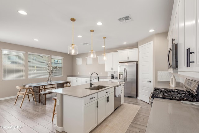 kitchen featuring appliances with stainless steel finishes, pendant lighting, sink, white cabinets, and a center island with sink