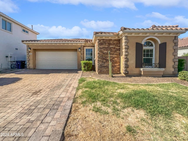 mediterranean / spanish-style home featuring a garage, stone siding, decorative driveway, stucco siding, and a front lawn