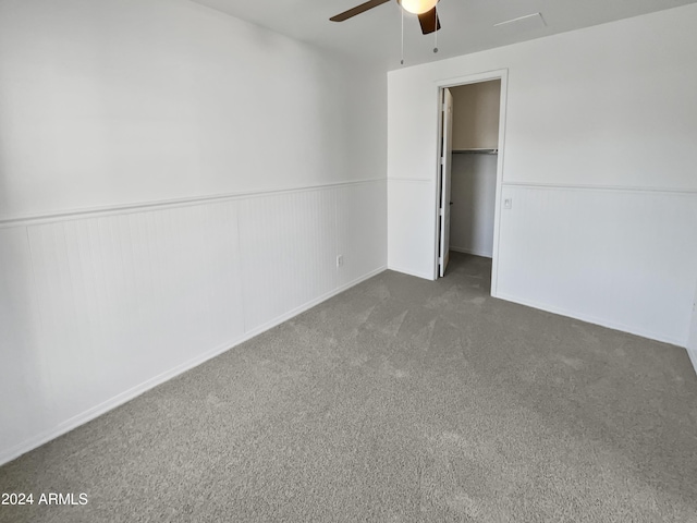 unfurnished bedroom with a wainscoted wall, a spacious closet, a closet, and dark carpet