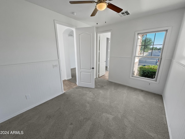 unfurnished bedroom with light colored carpet, a wainscoted wall, visible vents, and ceiling fan