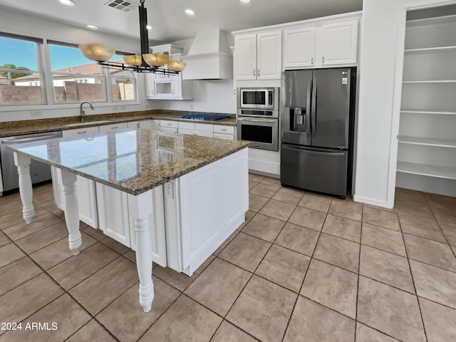 kitchen featuring a kitchen island, dark stone countertops, stainless steel appliances, premium range hood, and a sink