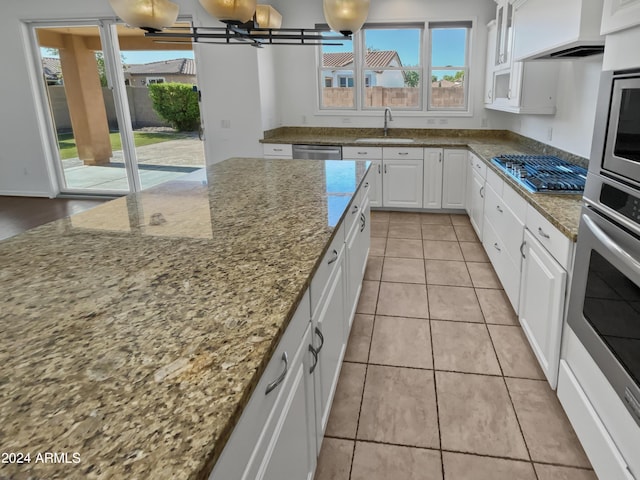 kitchen featuring white cabinets, appliances with stainless steel finishes, stone counters, premium range hood, and a sink