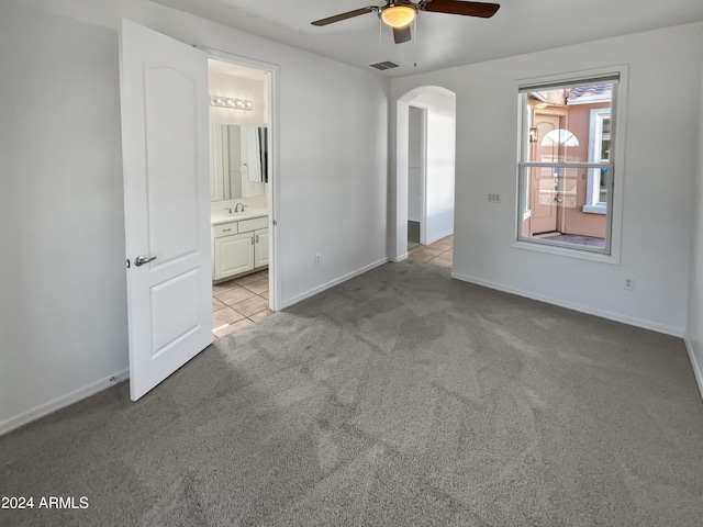 unfurnished bedroom featuring baseboards, visible vents, arched walkways, and light colored carpet