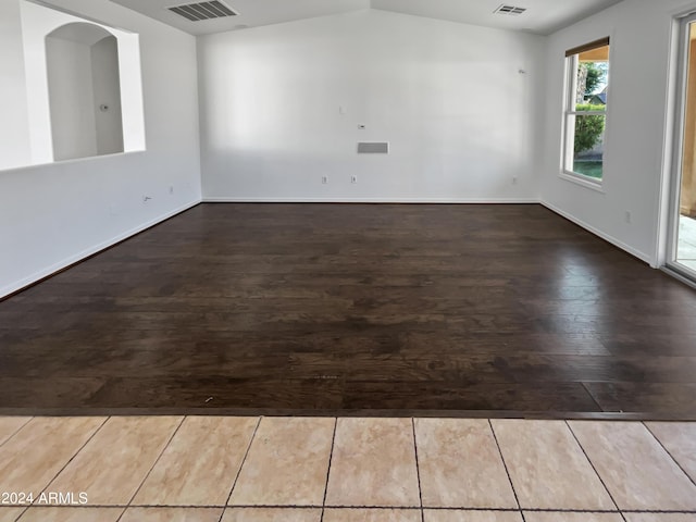 empty room with baseboards, visible vents, vaulted ceiling, and wood finished floors