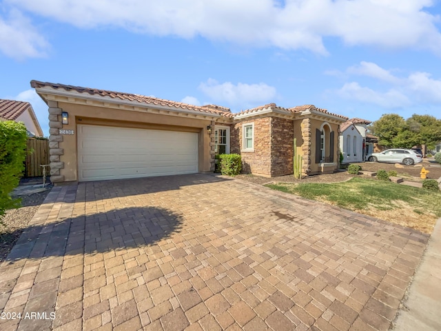 mediterranean / spanish house featuring a tiled roof, decorative driveway, an attached garage, and stucco siding