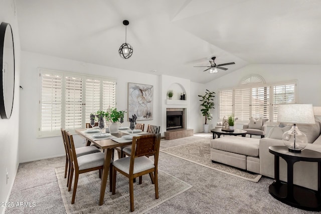 carpeted dining room featuring a healthy amount of sunlight, a fireplace, a ceiling fan, and lofted ceiling