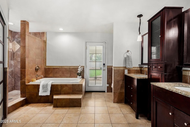 bathroom with two vanities, a garden tub, tile walls, and a sink