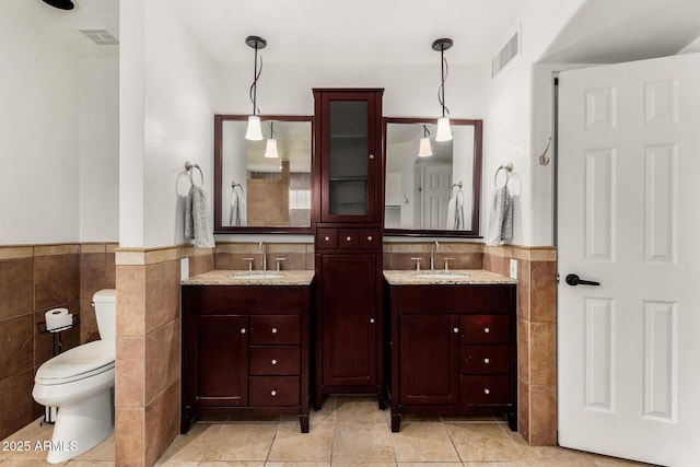 bathroom featuring a sink, visible vents, two vanities, and tile walls