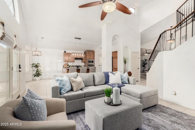 living room featuring a ceiling fan, a high ceiling, light tile patterned flooring, arched walkways, and stairs