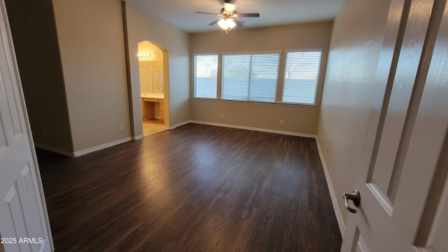 unfurnished bedroom with arched walkways, ensuite bath, dark wood-style floors, and baseboards