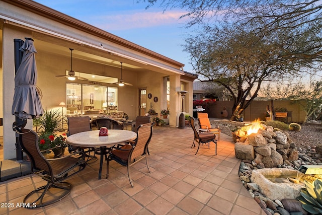 patio terrace at dusk with a grill, ceiling fan, and an outdoor fire pit