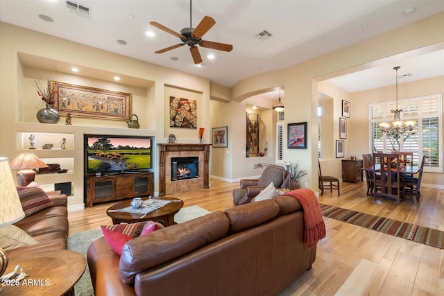 living room with ceiling fan with notable chandelier, light hardwood / wood-style floors, a fireplace, and built in shelves