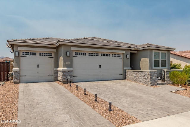 prairie-style home featuring a garage, stone siding, decorative driveway, and stucco siding