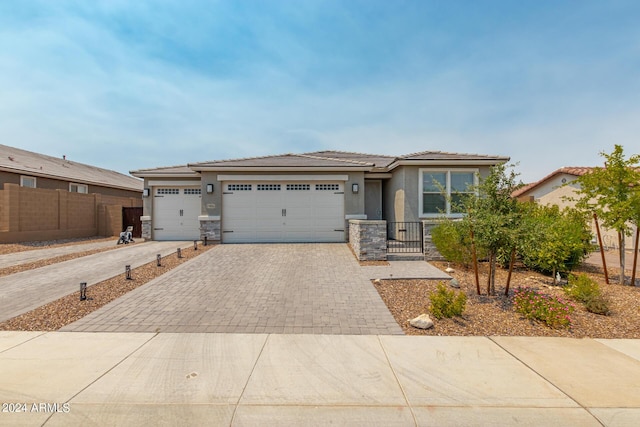 prairie-style house with a garage, fence, stone siding, decorative driveway, and stucco siding